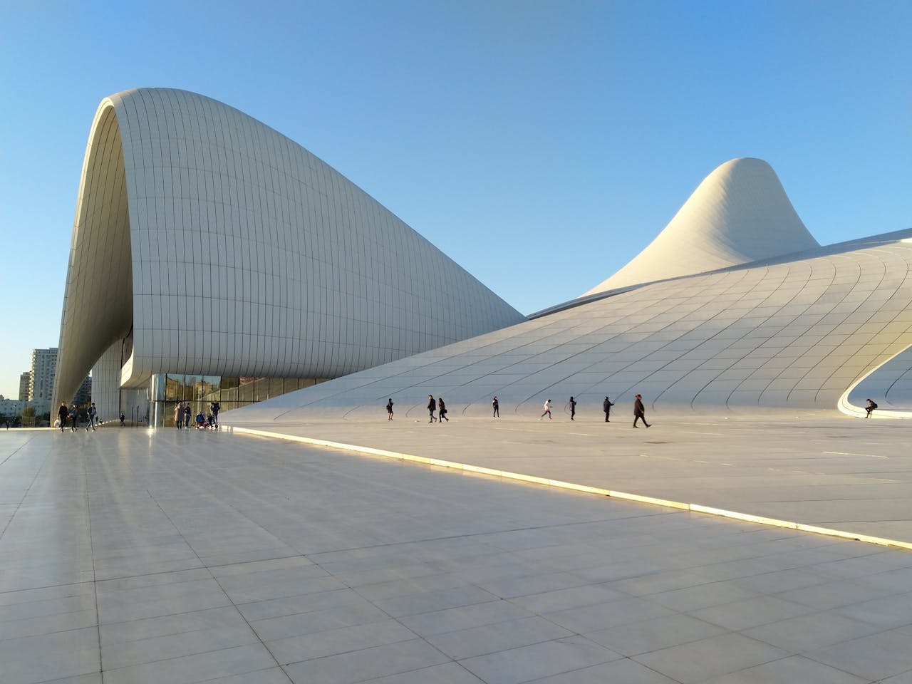Striking modern architecture of the Heydar Aliyev Center in Baku with people walking under clear skies.